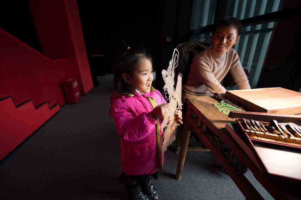 1月7日，在陕西西安明清皮影艺术博物馆，一名前来参观的小女孩拿起一幅先前雕刻好的皮影骨架。